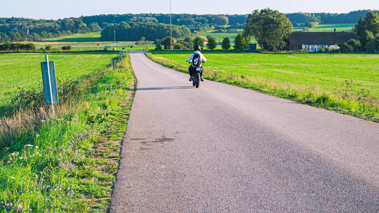 Ung person åker moped längs en somrig landsväg. 