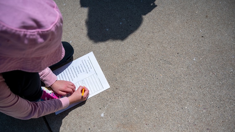 Barn fyller i ett formulär på marken. 